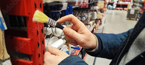 A customer holds a paint tray and brushes while shopping in a hardware store aisle. Concepts of home improvement, DIY renovation, consumer choice, and retail shopping behavior.