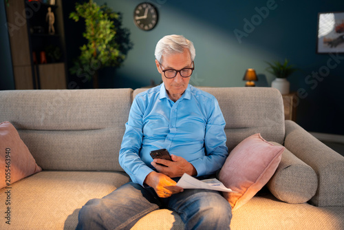 Konstfotografi Elderly man using smartphone to pay household utility bills through a mobile application at home
