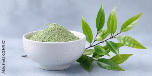 green tea powder in a white bowl with green leaves on the side, on a light grey background.