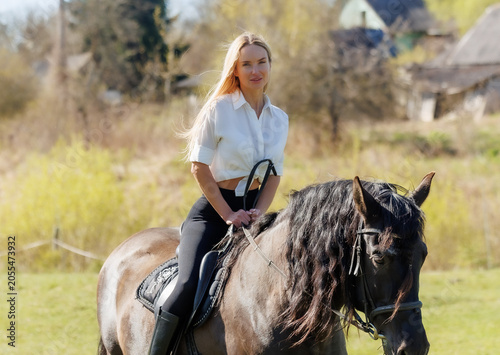 Young woman riding a black horse in spring countryside