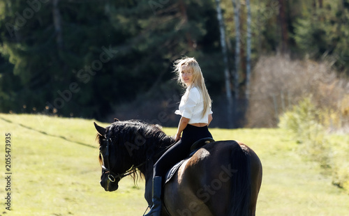 Young woman riding a black horse in spring countryside