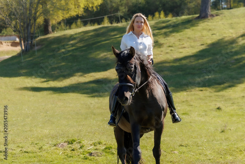 Young woman riding a black horse in spring countryside