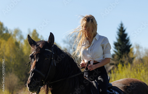 Young woman riding a black horse in spring countryside