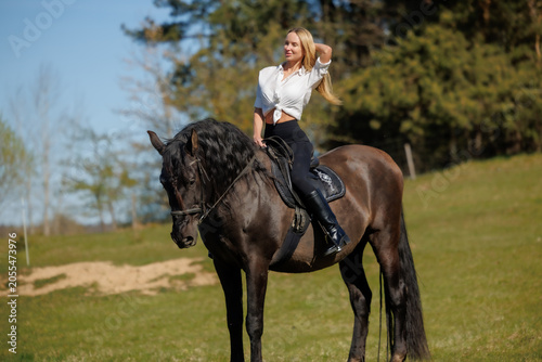 Young woman riding a black horse in spring countryside