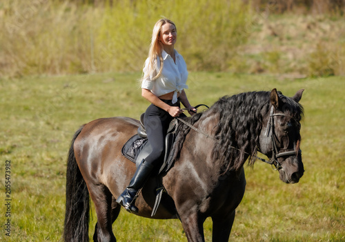 Young woman riding a black horse in spring countryside