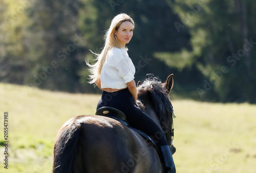 Young woman riding a black horse in spring countryside