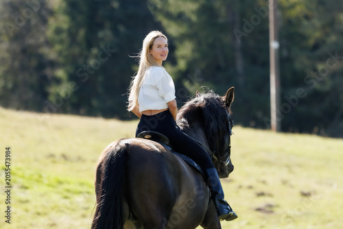 Young woman riding a black horse in spring countryside