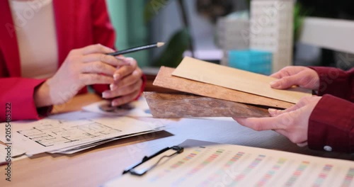 Customer holds wooden panel samples as designer gives advice in office. Female expert explains difference between lamber types to client slow motion