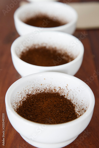 ground coffee in white ceramic bowls arranged in a row on a table for specialty coffee quality testing by Q grader. Coffee cupping, tasting and grading concept in a roastery or cafe. Selective focus.