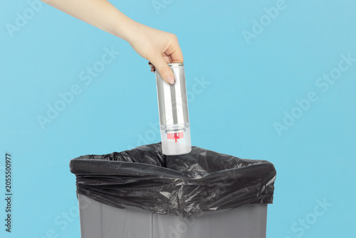 Throwing gas in a bottle for refilling lighters into the trash can, holding gas in a bottle in hand in front of the trash can.