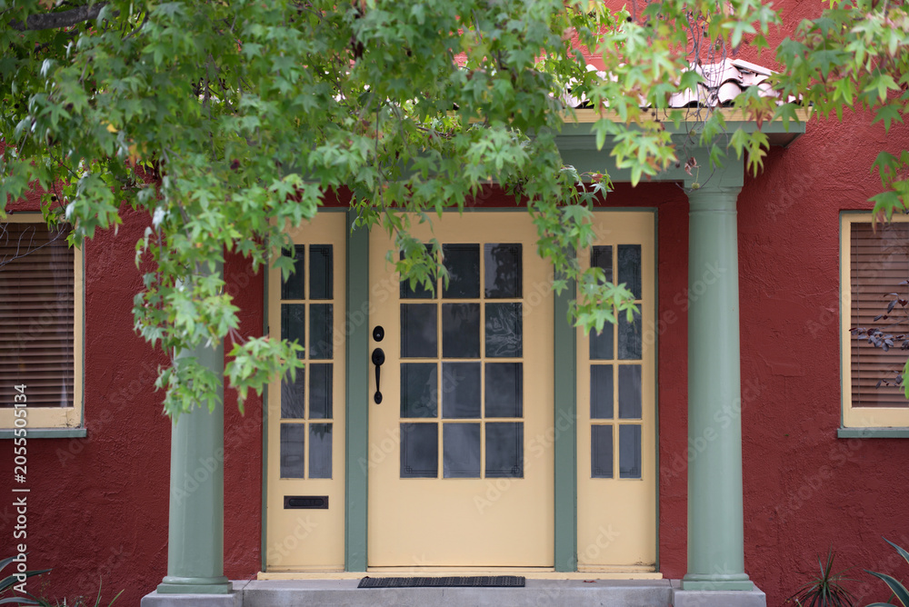 Naklejka premium Entrance with classic residential architecture details. Entrance with symmetrical facade and columns. Entrance framed by green leaves and porch. Entrance representing cozy suburban housing.