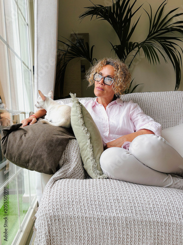 Woman with cat relaxing on a cozy sofa by a window, looking outside and enjoying a quiet moment at home