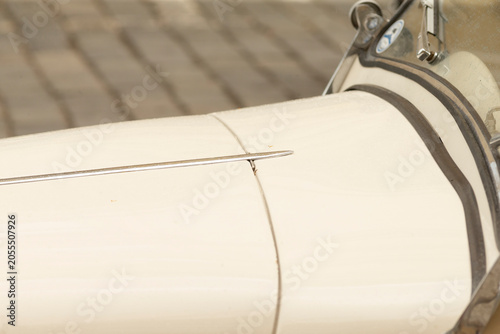 Cuadro en lienzo Tight detail of a metal sewing machine needle penetrating a smooth cream-colored fabric wrapped around a cylindrical drum