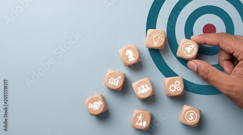 Hand selecting business strategy icon blocks on target board, highlighting wooden and management elements for modern business & office