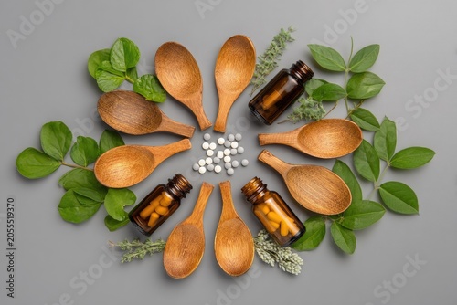 Wooden spoons arranged with leaves and medicine bottles on gray background