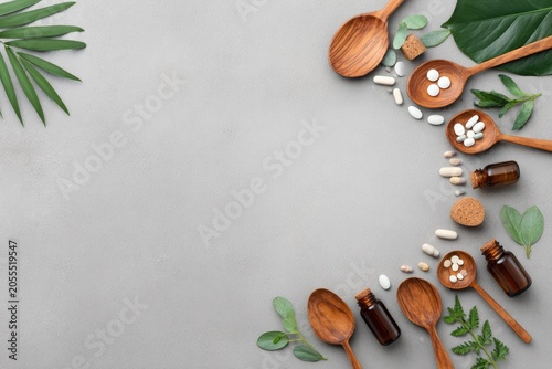 Wooden spoons with pills and herbs on grey background wellness concept