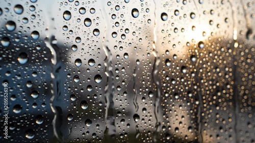 Close-up of rain drops on window glass with blurry outdoor background during sunset