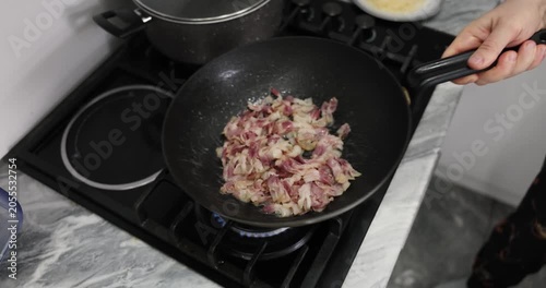 Experienced chef carefully stirs crispy bacon by shaking heavy frying pan. Juicy pork meat slowly becomes golden and crispy. Slow motion