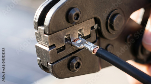 Crimping tool attaching metal terminal to electrical cable close up