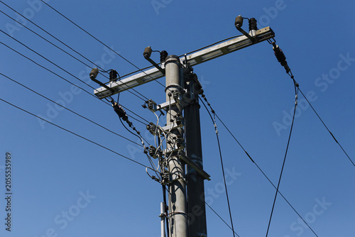 Electricity distribution pole with power lines against blue sky. Energy infrastructure and utility network. Electrical transmission equipment supplying homes and industry