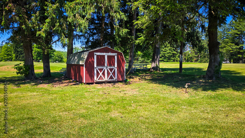 Red storage shed in a grassy field surrounded by trees