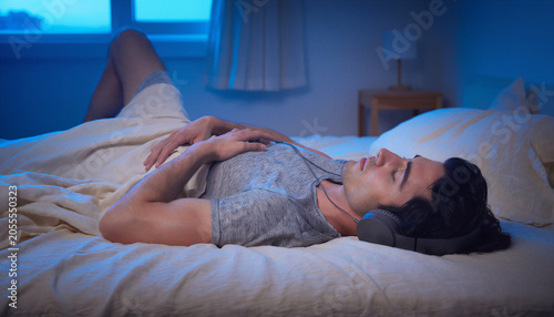 Young Man Sleeping on Bed with Headphones in Blue-Lit Bedroom at Night Lying on