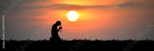 Photos A silhouette of a man kneeling in prayer against a dramatic sunset, with the sun
