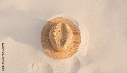 Woven straw fedora hat resting crown-down on smooth white sand in warm golden su