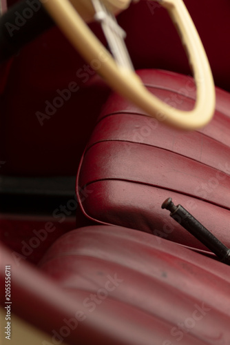 Tight view of a classic car cabin featuring worn burgundy leather bench seats, a black handbrake lever, and an ivory steering wheel rim. Soft directional