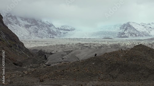 People walking on Jokulsarlon glacier under moody skies and mountains