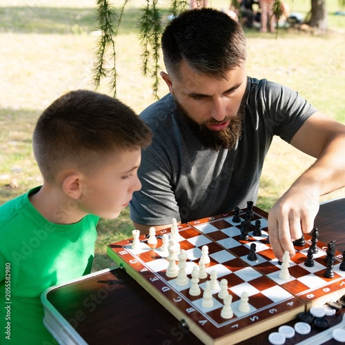 A father and son enjoy a sunny afternoon playing chess outdoors.
