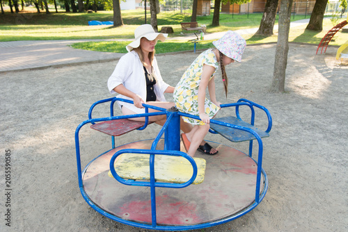 A mother and daughter enjoy a sunny day at the playground, sharing a ride on a merry-go-round.
