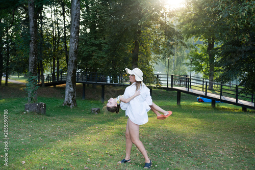 A woman playfully holds her daughter upside down in a sunlit park. Pure joy and carefree fun.
