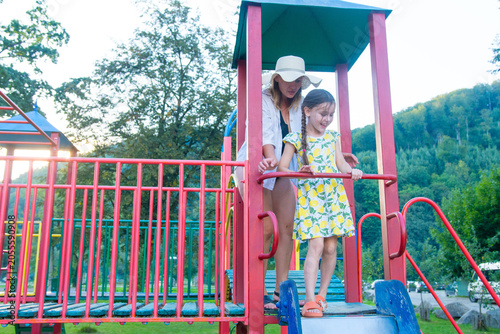 A mother and daughter enjoy a sunny day at the playground, sharing a moment of playful fun on the slide.