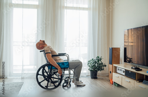 unhappy sad man in wheelchair sitting alone in living room leaning head back in frustration or exhaustion representing depression fatigue mental health challenges and struggles of disability