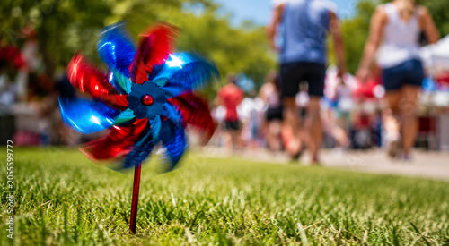 Obraz na plátně Red white and blue pinwheel spins in grass, blurred background of people celebrating, festive summer day