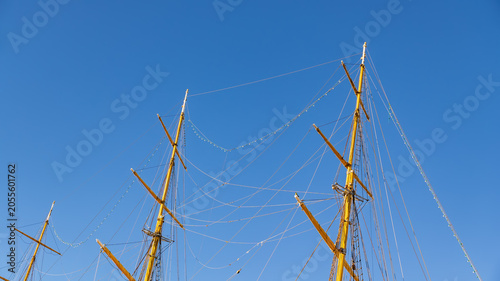 Quadro su tela Majestic yellow masts of a tall sailing ship reaching into a clear, solid blue s