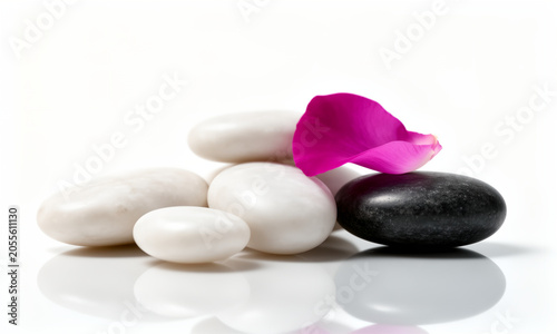 A stack of smooth white and black spa stones with a vibrant pink rose petal.