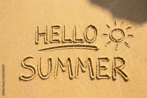 Hello summer written in sand on beach, playful sun drawing nearby, relaxing vacation concept, warm sunny weather greeting.
