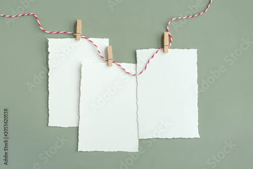 Tableau sur toile Close-up shot of white blank sheets of watercolor paper with torn edges suspended on decorative rope using small wooden clothespins on a gray board