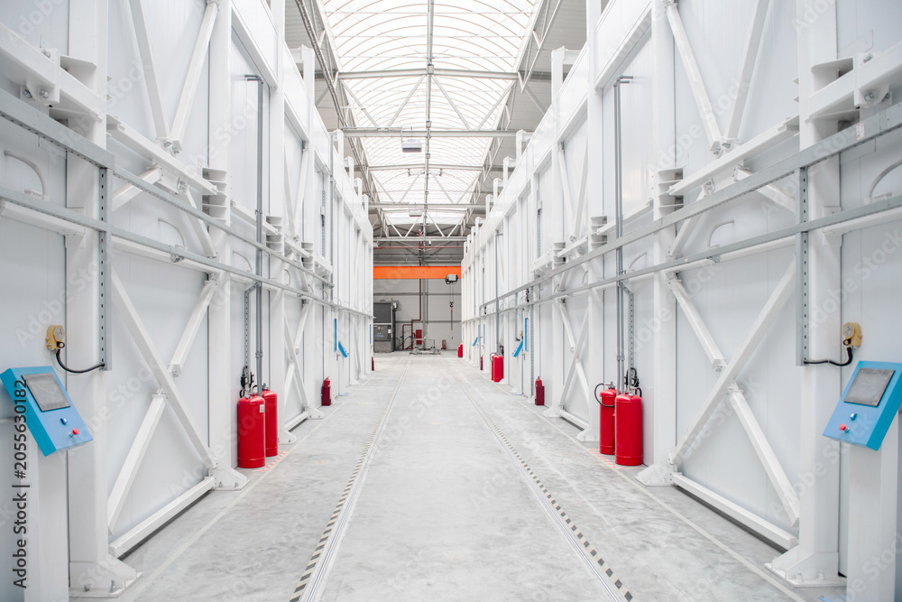 Fototapeta premium Long white warehouse corridor with red fire extinguishers