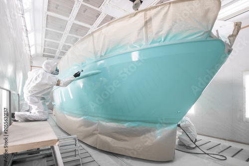 Worker in full gear paints boat with light blue finish