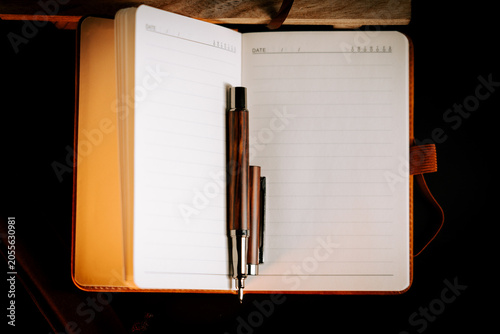Open notebook with brown pen poised to write on a dark table surface