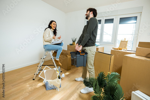 Cuadro en lienzo A young woman sitting on a stepladder while a man holds a heavy toolbox during r