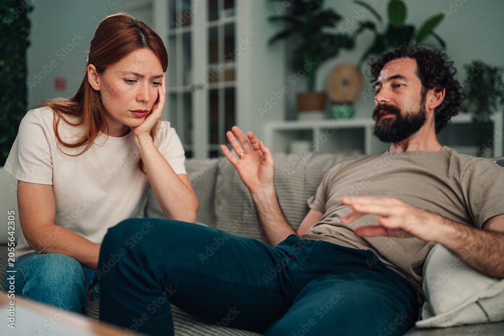 Fototapeta premium Couple discussing relationship problems at home, woman looking unhappy, man explaining disagreement