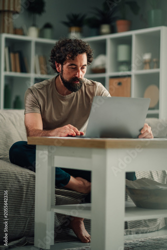 Принти на полотні Man working remotely from living room, concentrating on laptop screen, embracing