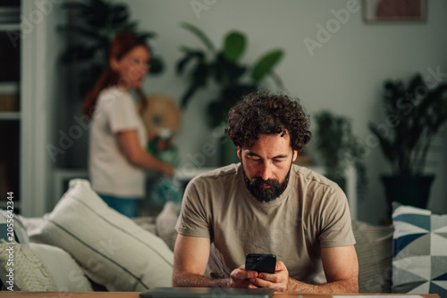 Fotografía Man ignoring partner, focused on smartphone, showing digital addiction and relat