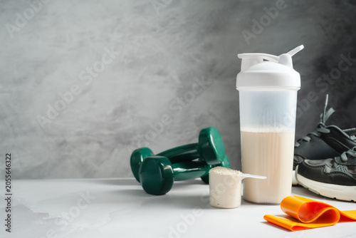 Protein shake and whey powder with dumbbells and running shoes, fitness nutrition concept, copy space