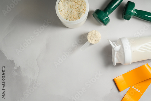 Protein shake and fitness equipment on gray background, sports nutrition flat lay
