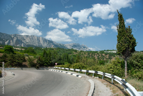 Winding mountain road with barrier and scenic view of rocky peaks and green valley